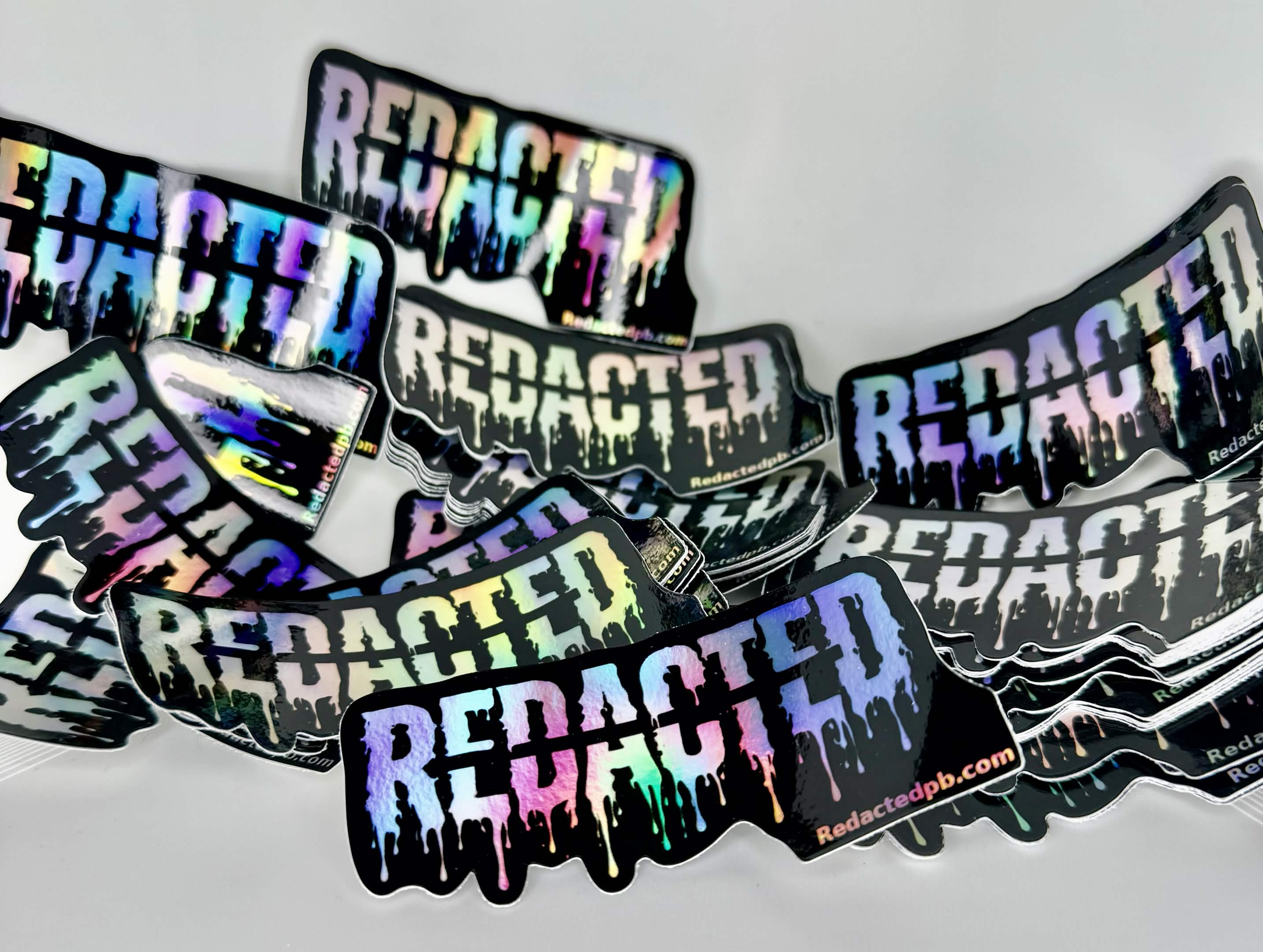 Holographic 'REDACTED' stickers on a white background