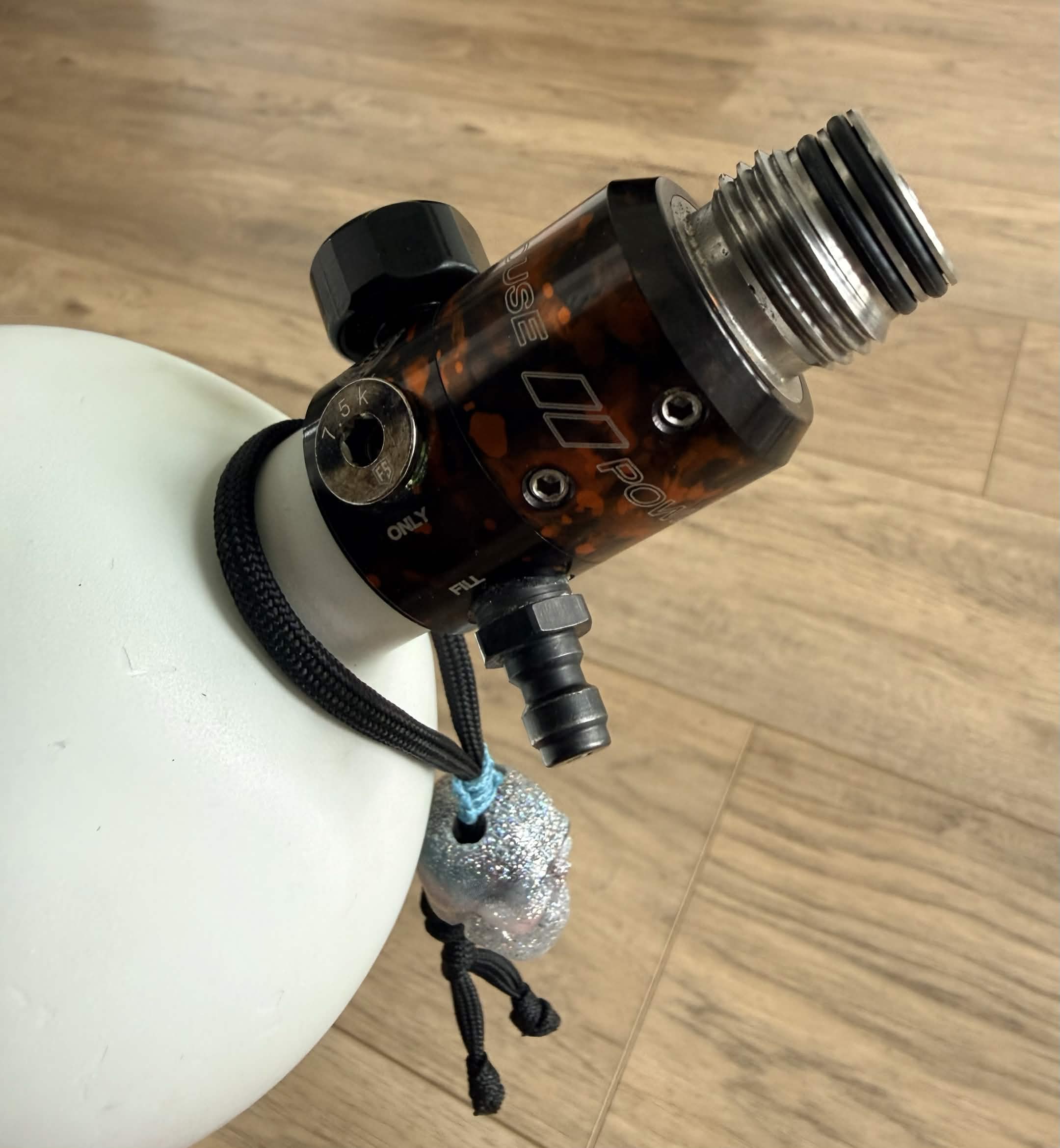 Handmade [REDACTED] frag tag hanging from white paintball air tank on wood floor background