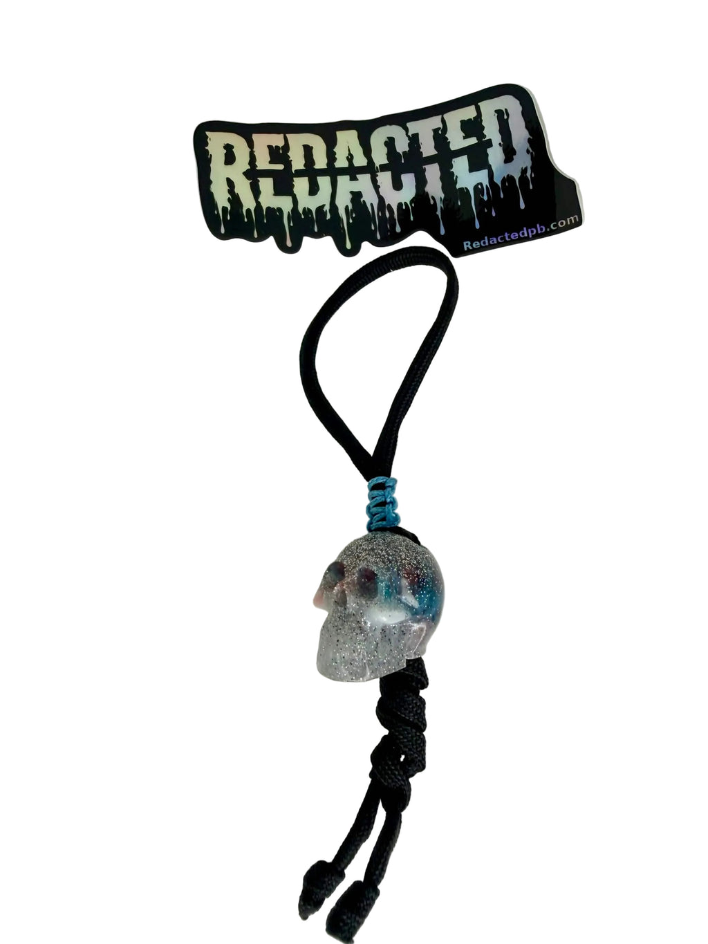 Keychain with skull design and 'REDACTED' branding on a white background