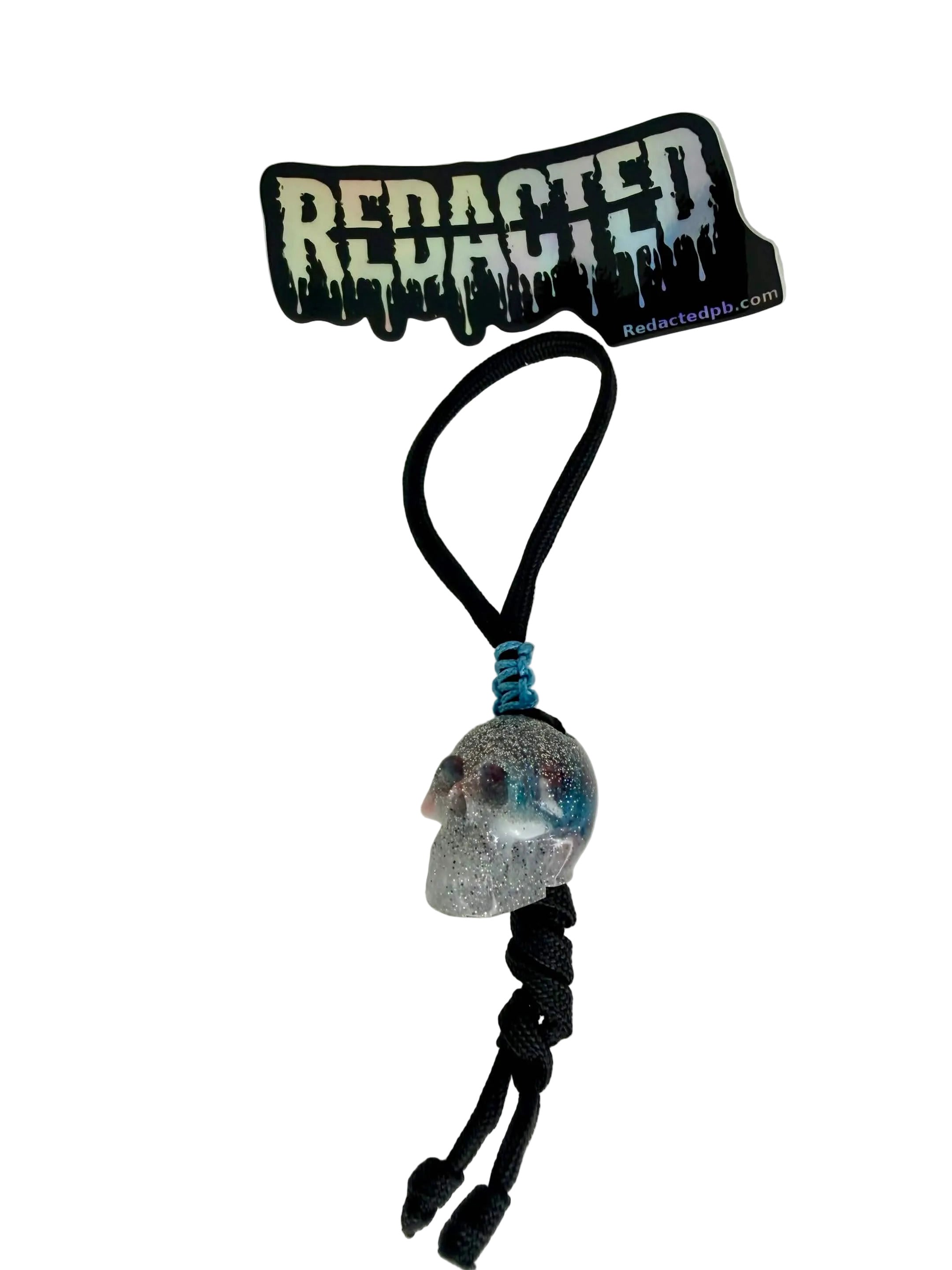 Keychain with skull design and 'REDACTED' branding on a white background