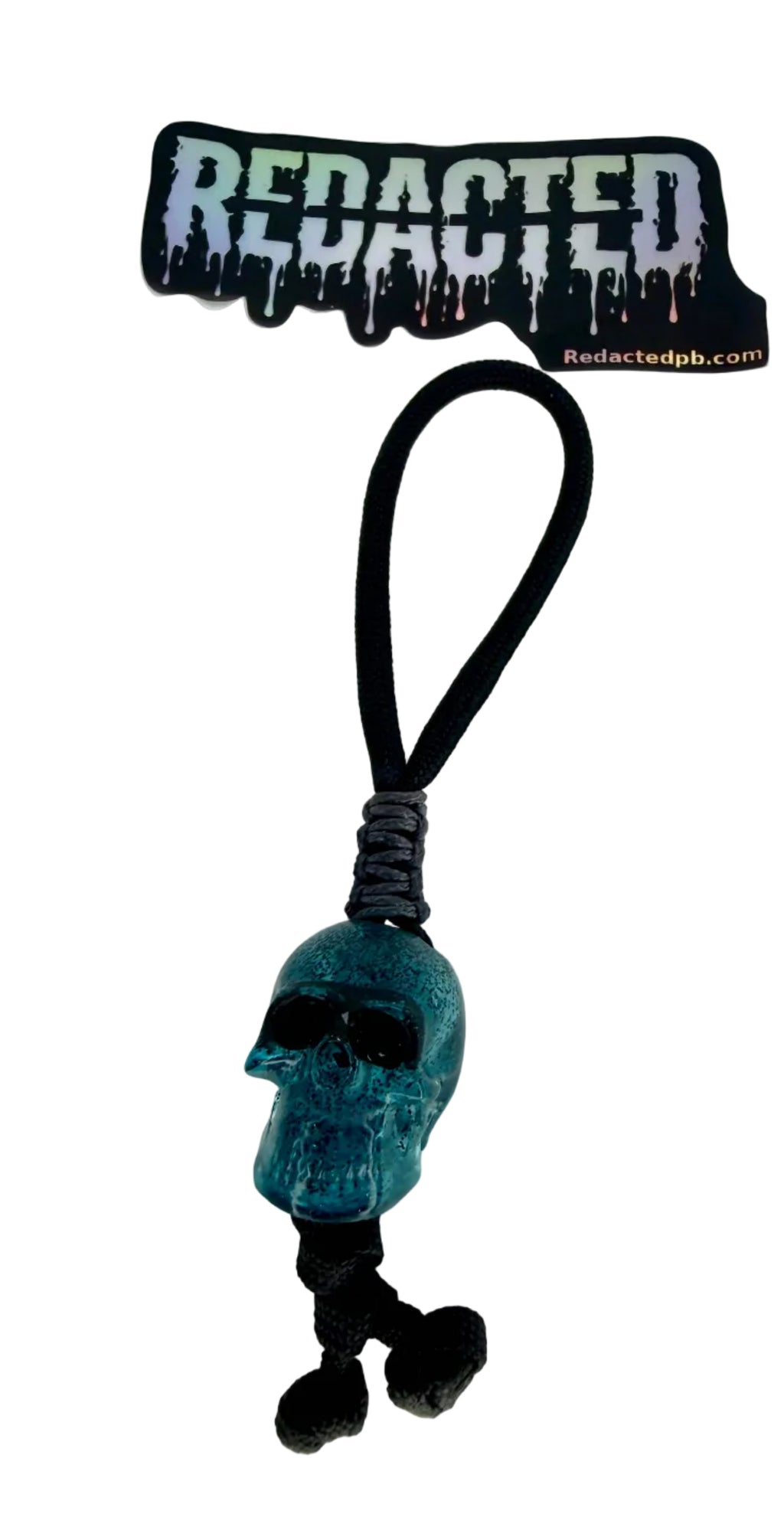 Blue skull charm on a black cord with 'REDACTED' label above on a white background